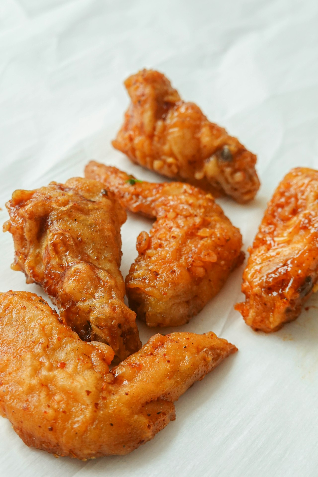 Glazed chicken wings rest on white paper.