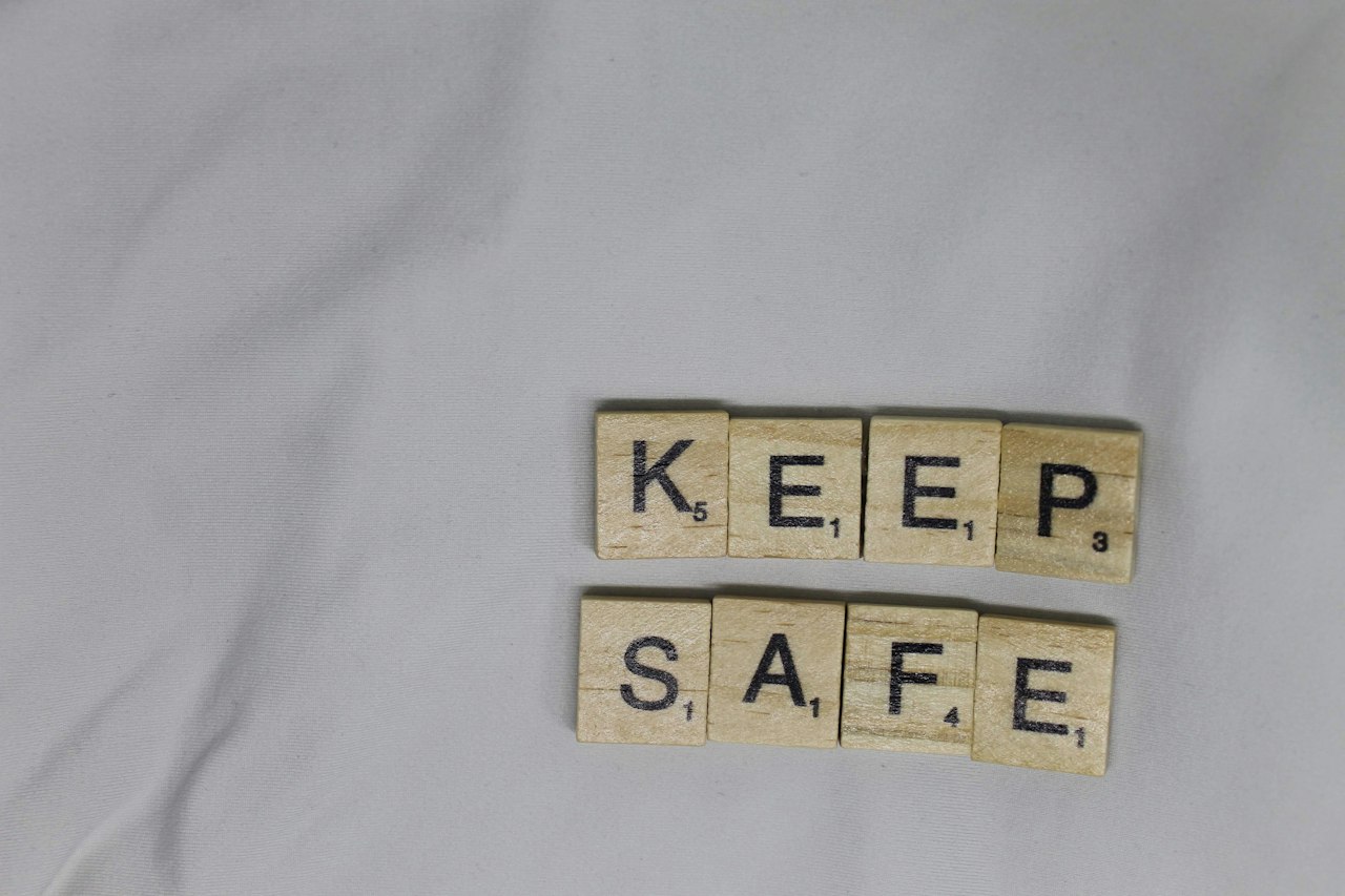 Wooden letter tiles spell KEEP SAFE on light gray fabric.