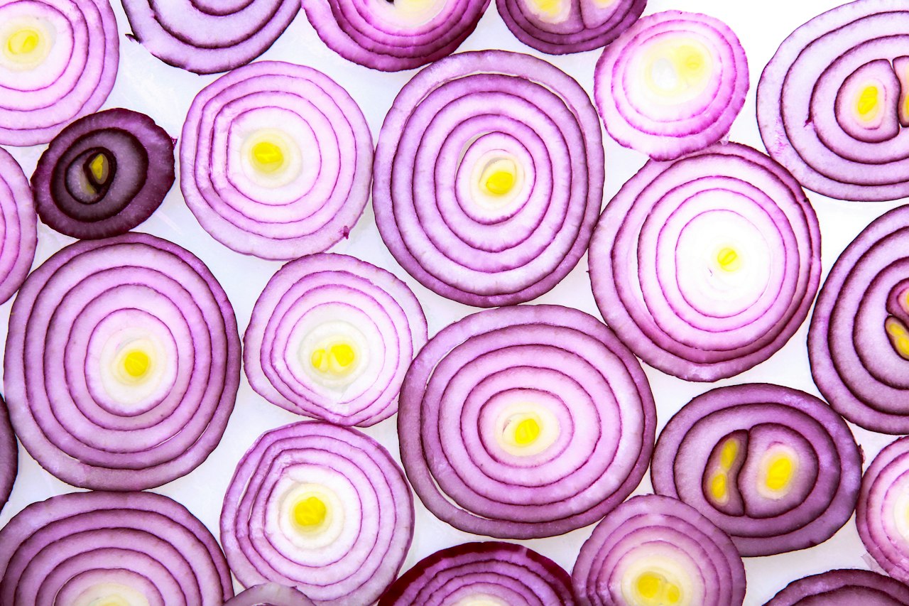 Thin overlapping red onion cross-sections cover a white surface.