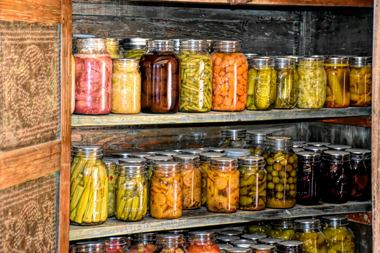 Wooden cupboard shelves hold glass jars filled with foods of different colors.