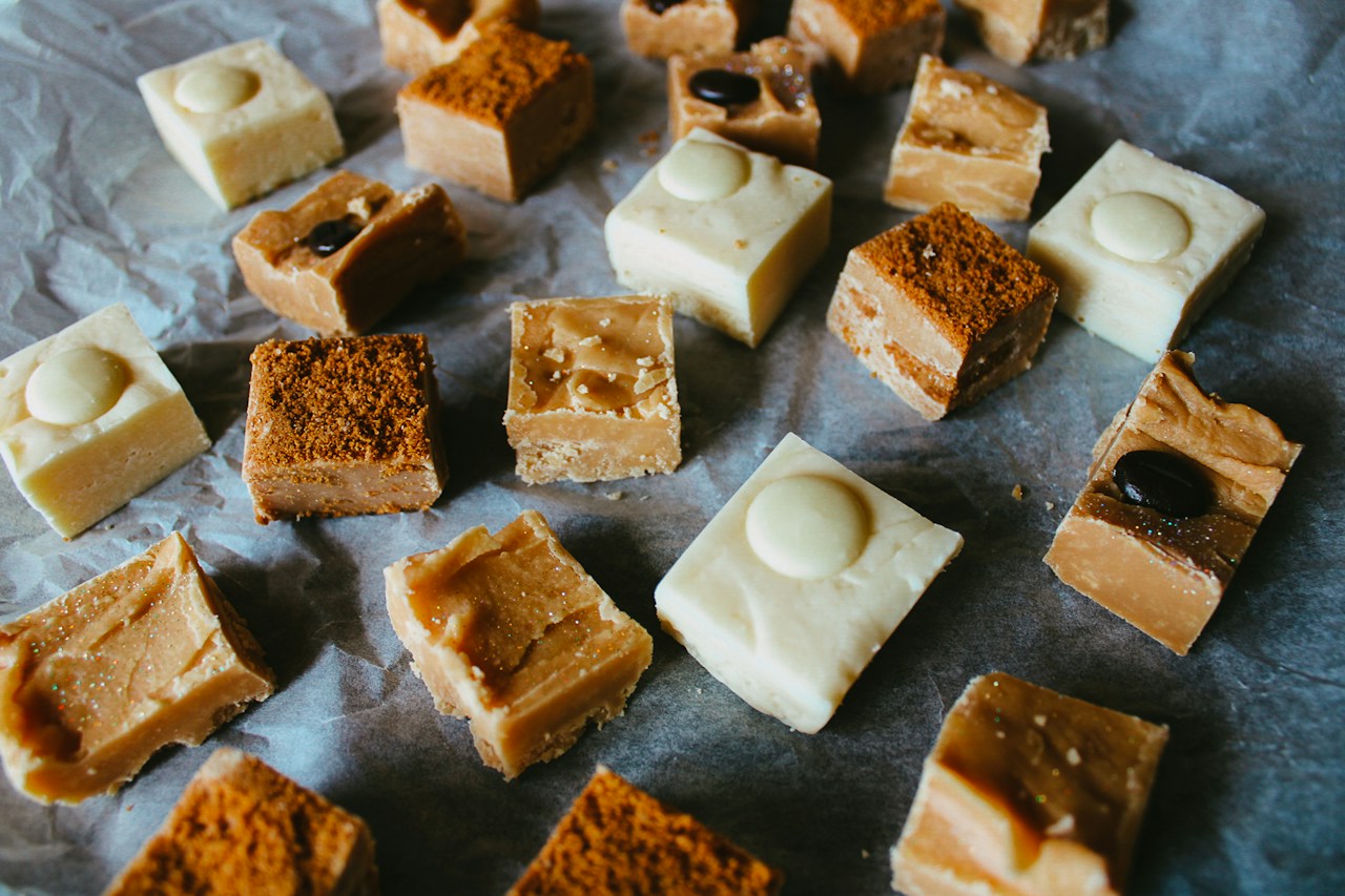 Small pale and caramel-colored fudge squares with assorted toppings sit on crinkled parchment.