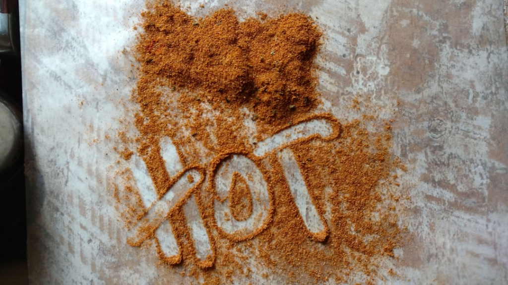The word HOT is traced in brown spice powder on a pale surface.
