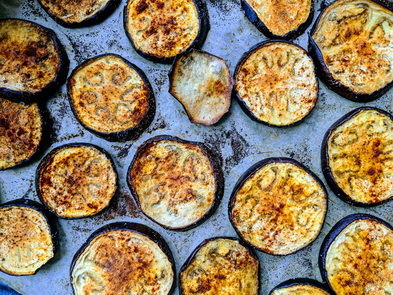 Browned eggplant rounds cover a dark baking tray.