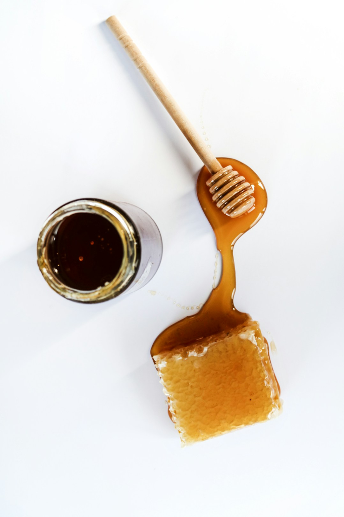 Honeycomb, a honey dipper and a glass jar on a light background.