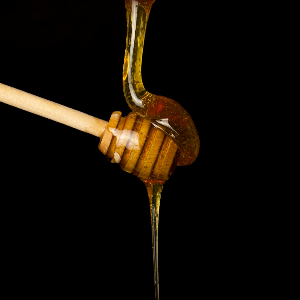 Honey flowing onto a wooden dipper against a black background.
