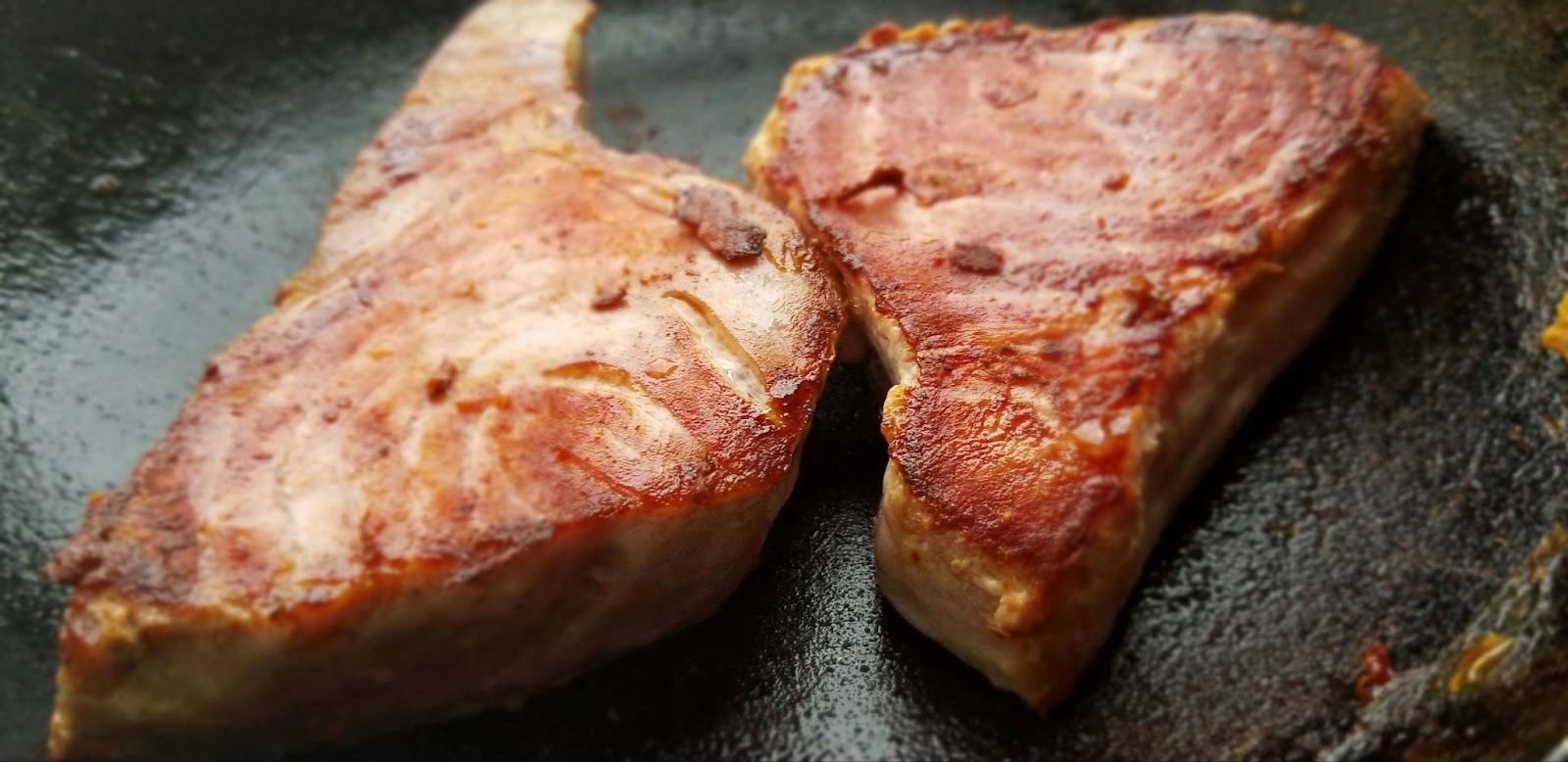 Two seared fish steaks in a pan.