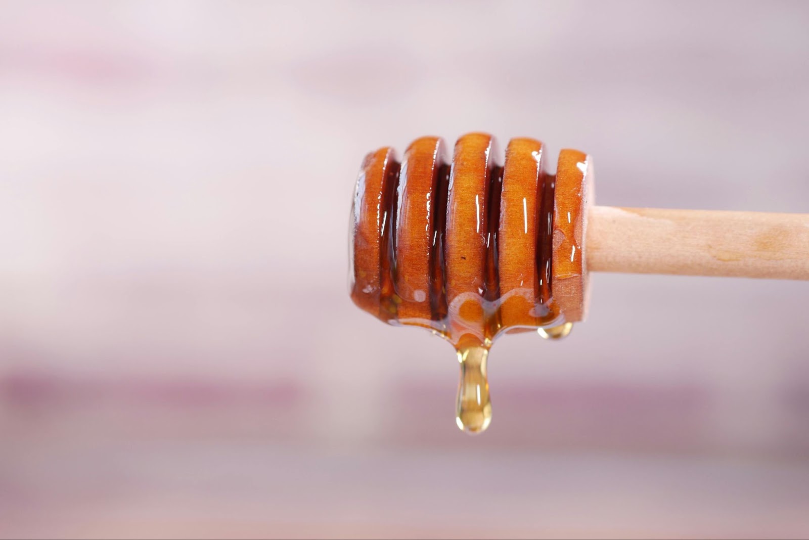 Honey dripping from a wooden dipper against a pale background.